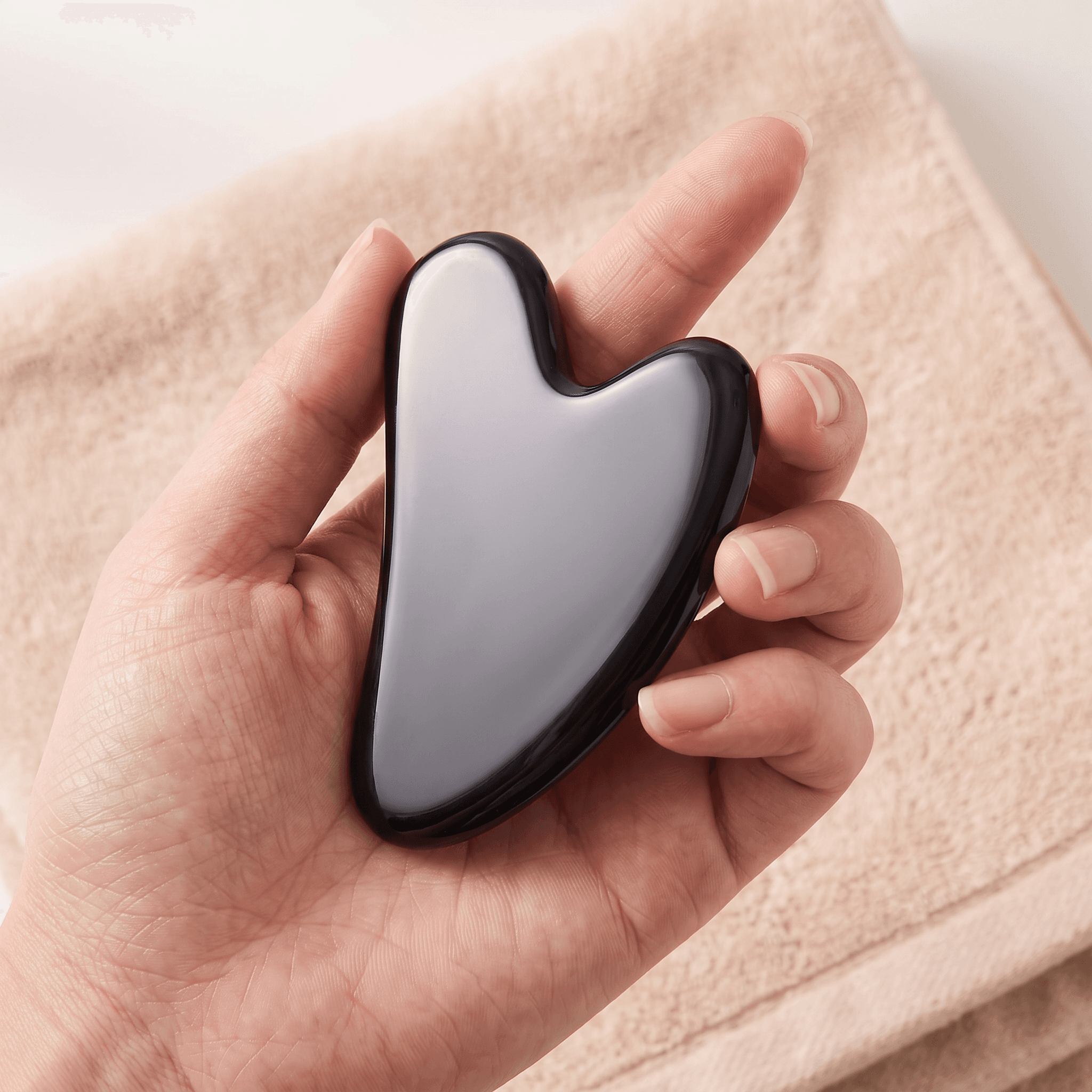 The black gua sha held in a hand to show its size and finish.